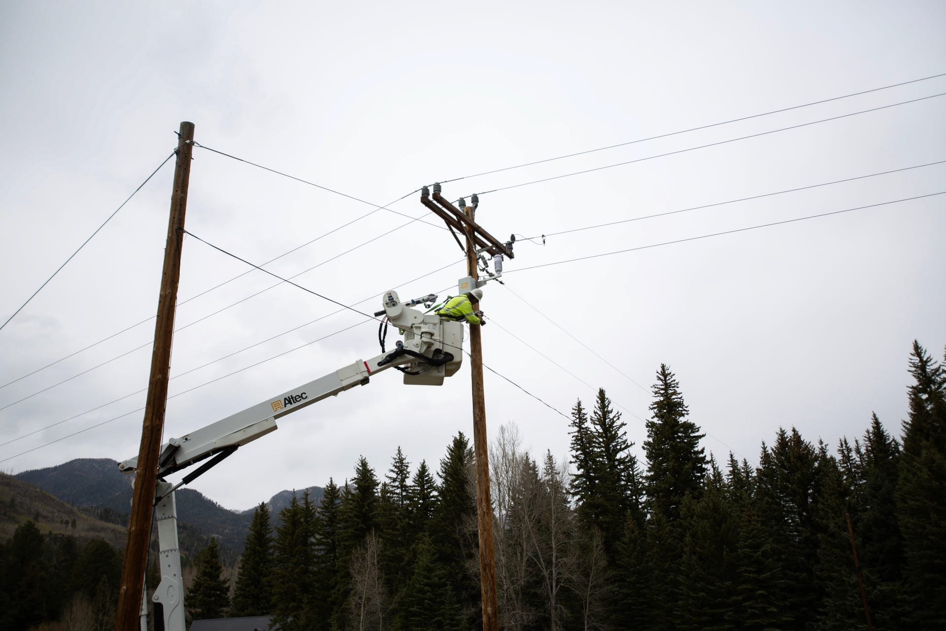 Bucket truck lifting a lineman to service a utility pole with a WatchPost weather station, forested mountains behind
